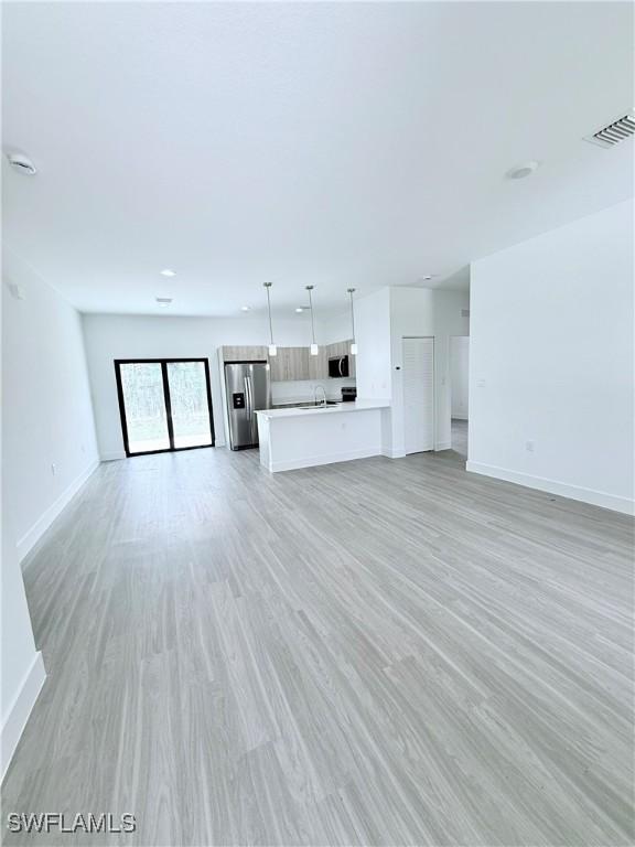 unfurnished living room with baseboards, light wood-style floors, and visible vents