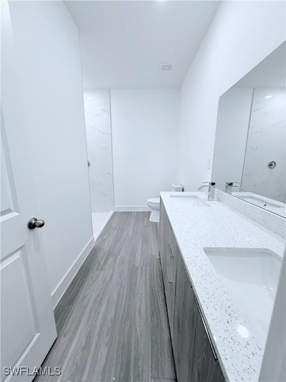 bathroom featuring visible vents, double vanity, wood finished floors, toilet, and a sink