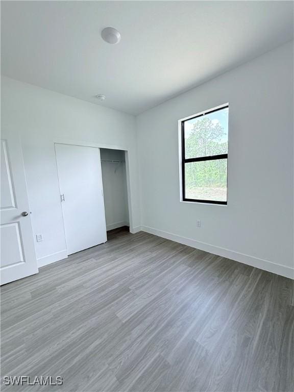 unfurnished bedroom with baseboards, wood finished floors, and a closet