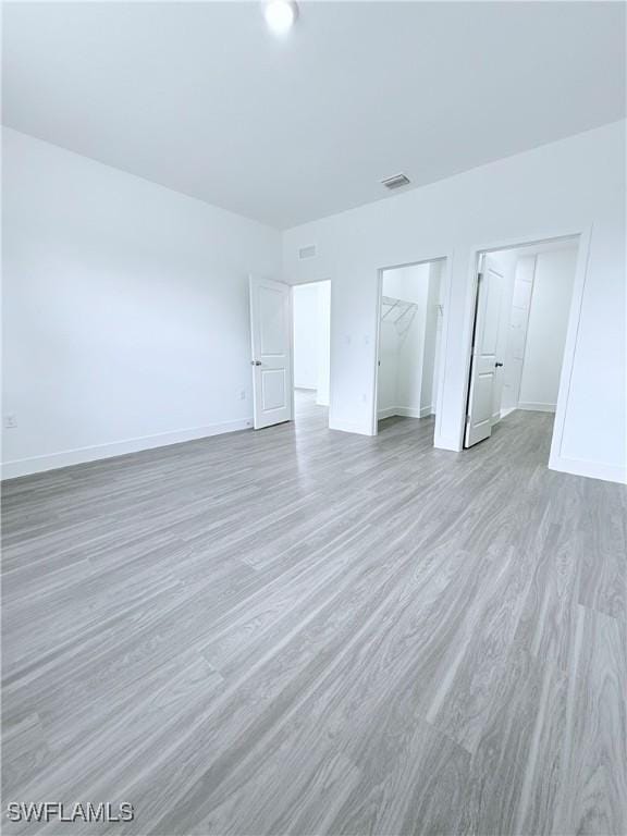 unfurnished bedroom with baseboards, a closet, wood finished floors, and visible vents