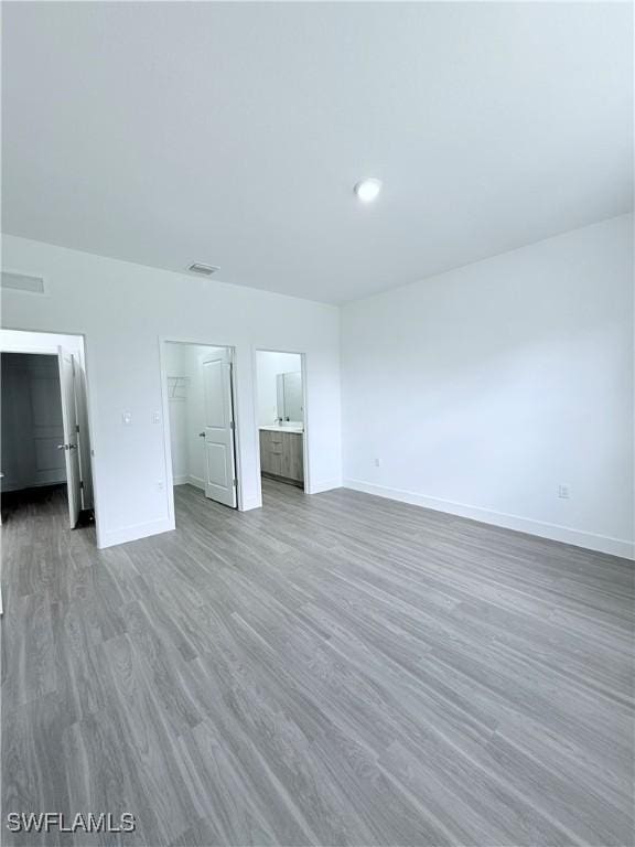 unfurnished bedroom featuring a closet, wood finished floors, baseboards, a spacious closet, and ensuite bath