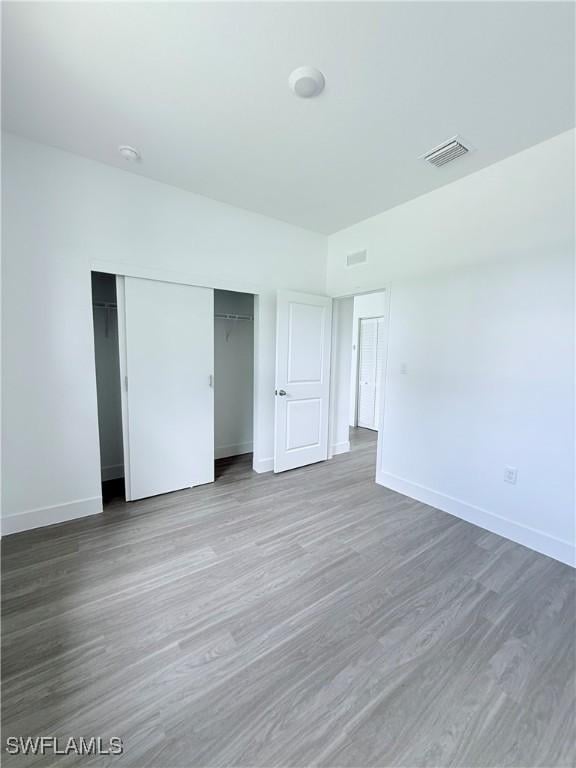 unfurnished bedroom with visible vents, baseboards, wood finished floors, and a closet