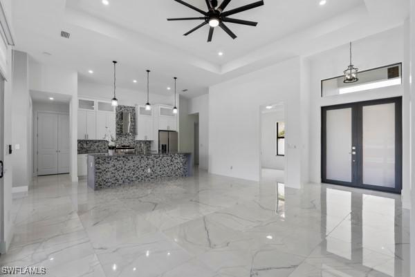 unfurnished living room featuring a raised ceiling, a towering ceiling, recessed lighting, a ceiling fan, and light marble finish floors