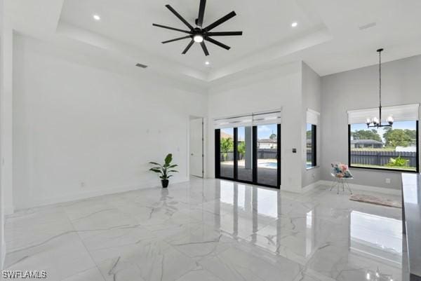 empty room featuring a high ceiling, a raised ceiling, marble tiled floors, a chandelier, and ceiling fan
