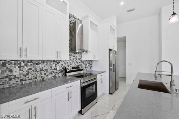 kitchen featuring stainless steel appliances, a sink, wall chimney exhaust hood, white cabinetry, and decorative backsplash