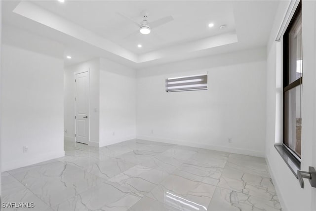 empty room with a raised ceiling, recessed lighting, baseboards, and light marble finish flooring