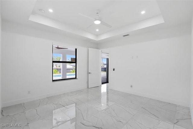 spare room featuring a ceiling fan, a tray ceiling, baseboards, recessed lighting, and light marble finish floors
