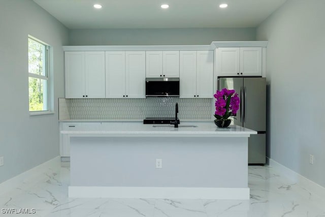 kitchen featuring freestanding refrigerator, a kitchen island with sink, baseboards, white cabinetry, and recessed lighting