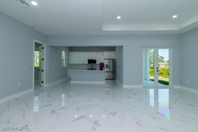 unfurnished living room featuring recessed lighting, baseboards, a raised ceiling, a sink, and light marble finish floors