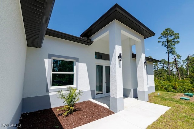 property entrance with stucco siding, french doors, and a yard