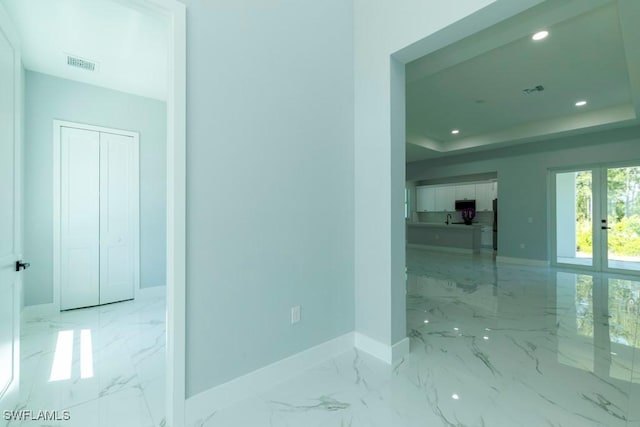 corridor featuring french doors, marble finish flooring, baseboards, recessed lighting, and a raised ceiling