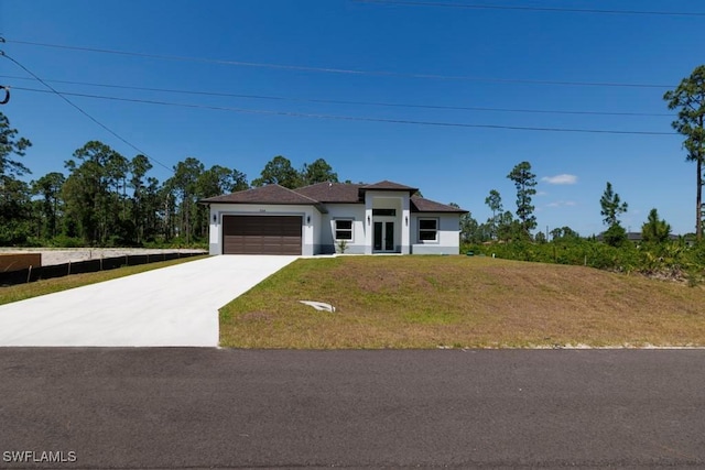 prairie-style house featuring concrete driveway, an attached garage, stucco siding, and a front yard