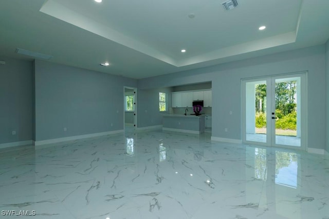 unfurnished living room with a raised ceiling, recessed lighting, baseboards, french doors, and a sink