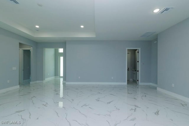 spare room featuring recessed lighting, baseboards, a raised ceiling, and light marble finish floors