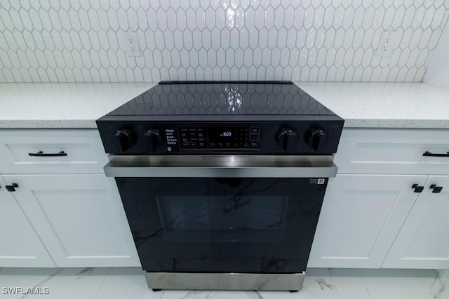 detailed view of electric range oven, decorative backsplash, white cabinets, and light stone countertops