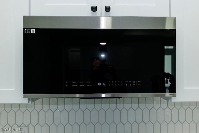 kitchen view of stainless steel microwave, tasteful backsplash, and white cabinets