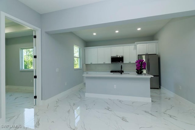 kitchen featuring appliances with stainless steel finishes, a sink, white cabinets, baseboards, and an island with sink