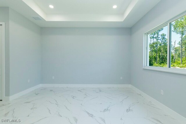 unfurnished room featuring a tray ceiling, recessed lighting, baseboards, and marble look tile flooring