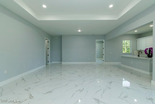 unfurnished room featuring recessed lighting, baseboards, a tray ceiling, and a sink
