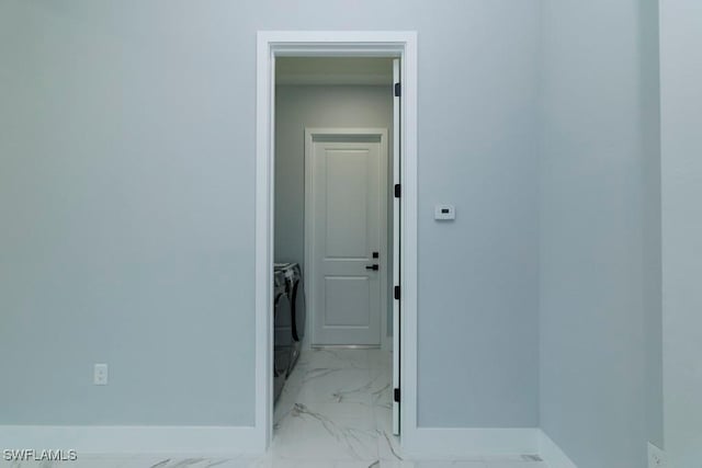 hallway with washing machine and dryer, baseboards, and light marble finish floors