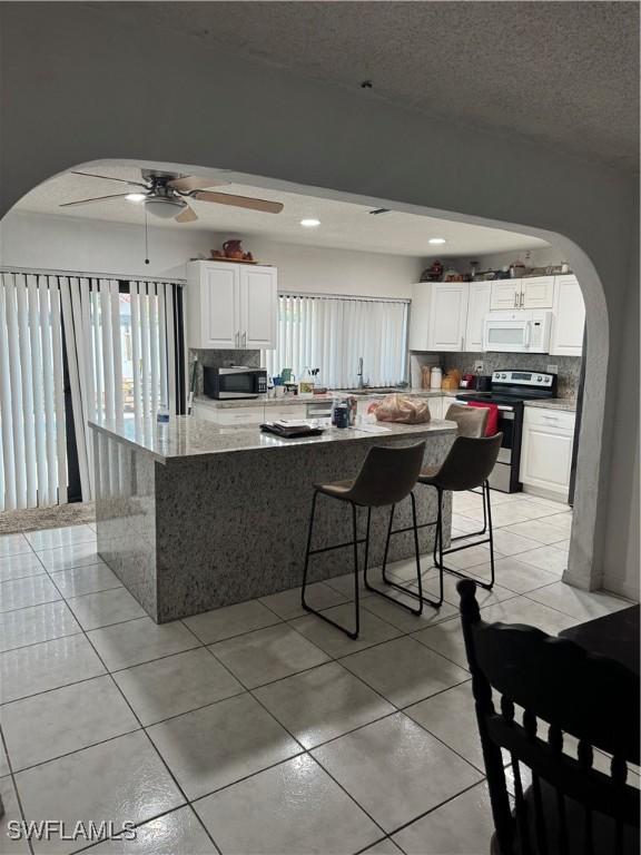 kitchen featuring backsplash, stainless steel appliances, arched walkways, and a ceiling fan