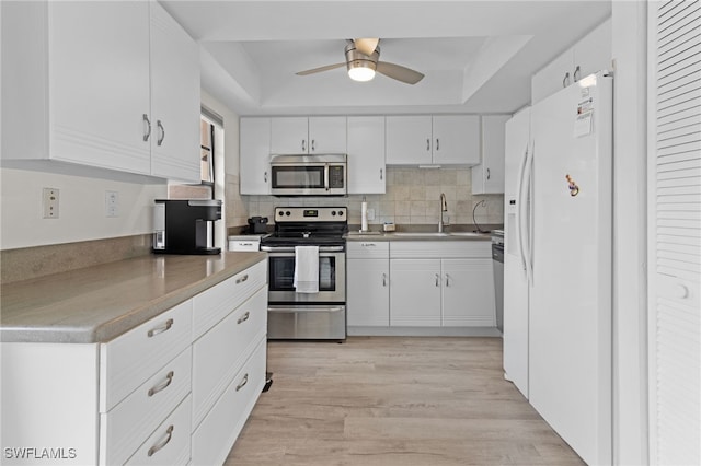 kitchen featuring white cabinets, stainless steel appliances, a sink, and a raised ceiling