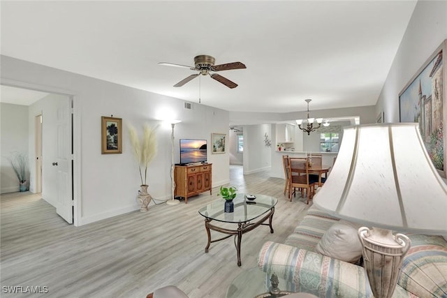 living room with baseboards, light wood-style flooring, and ceiling fan with notable chandelier