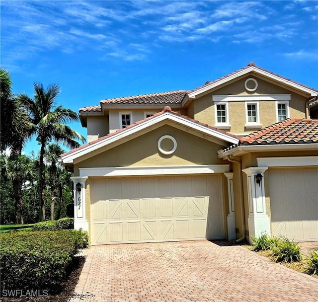 mediterranean / spanish home with stucco siding, a tile roof, an attached garage, and decorative driveway