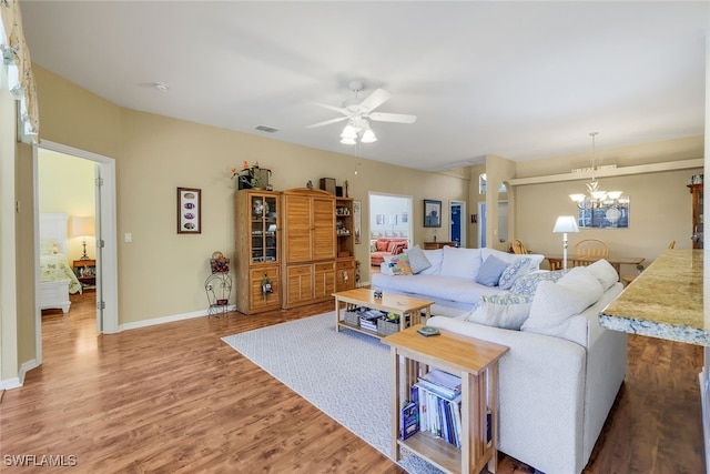 living area with baseboards, ceiling fan with notable chandelier, wood finished floors, and visible vents