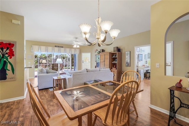 dining space with arched walkways, baseboards, wood finished floors, and ceiling fan with notable chandelier