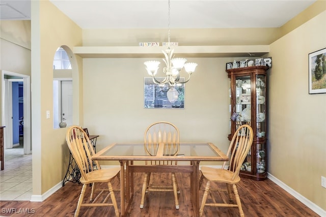 dining space with baseboards, arched walkways, wood finished floors, and a notable chandelier
