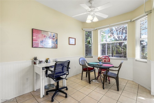 tiled dining room with ceiling fan and a wainscoted wall