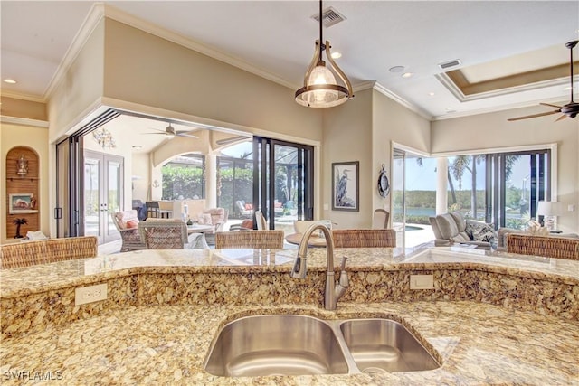kitchen with a ceiling fan, visible vents, a sink, light stone counters, and open floor plan