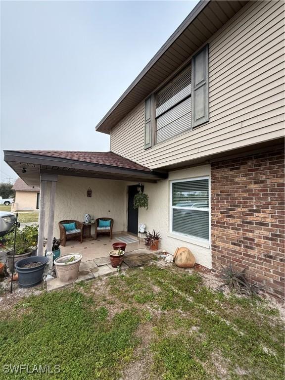 rear view of house featuring brick siding, a patio, a yard, and stucco siding