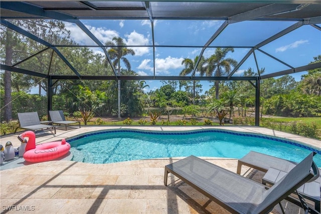 swimming pool with a patio, glass enclosure, and view of wooded area