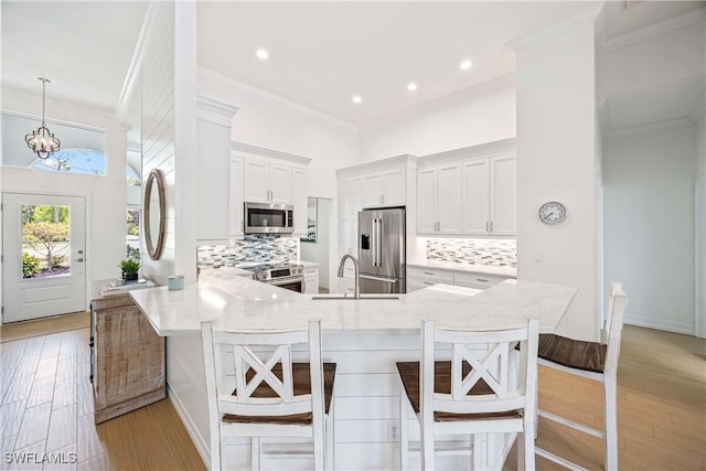 kitchen with stainless steel appliances, a sink, ornamental molding, white cabinets, and a peninsula