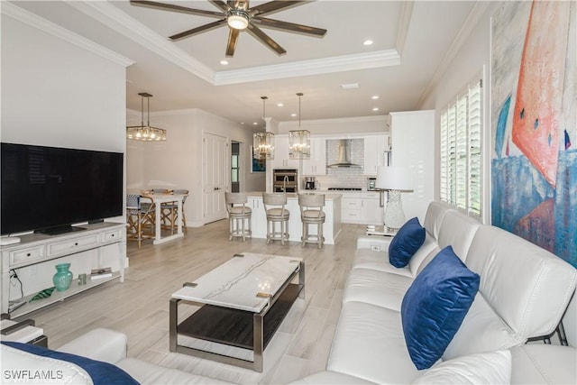 living area with a raised ceiling, ceiling fan, ornamental molding, light wood finished floors, and recessed lighting