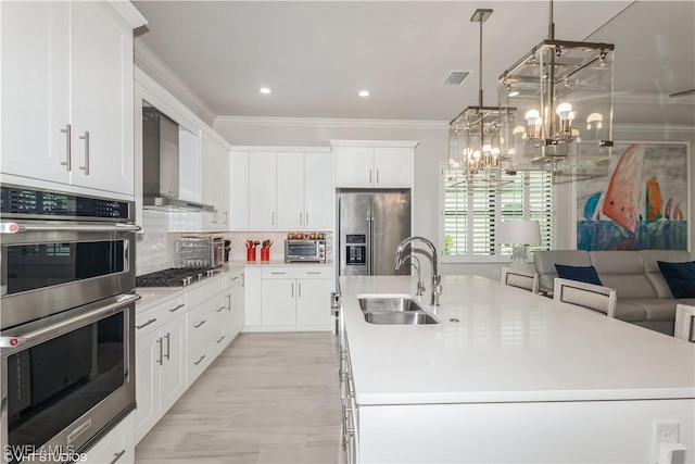 kitchen featuring wall chimney exhaust hood, appliances with stainless steel finishes, a sink, ornamental molding, and a center island with sink