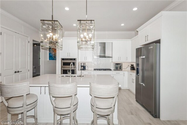 kitchen with appliances with stainless steel finishes, wall chimney range hood, a sink, light countertops, and white cabinets