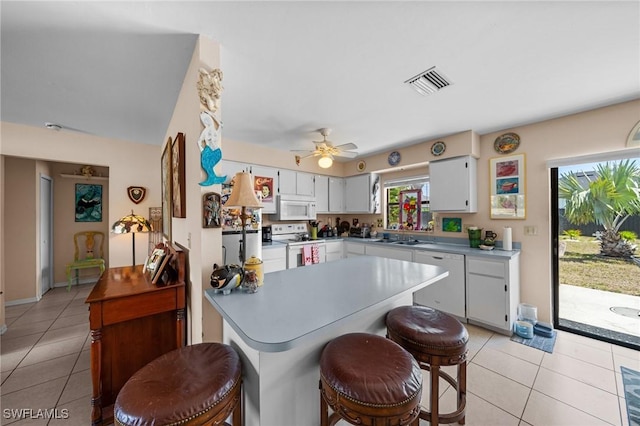 kitchen with white appliances, light tile patterned floors, light countertops, a ceiling fan, and a kitchen breakfast bar
