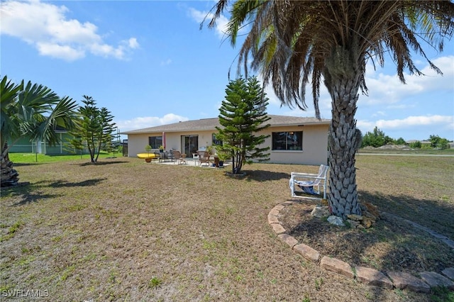 rear view of property with stucco siding, a lawn, and a patio