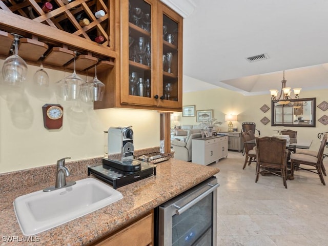 kitchen with an inviting chandelier, a sink, beverage cooler, visible vents, and glass insert cabinets