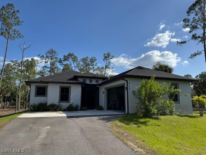 prairie-style home featuring an attached garage, a front lawn, stucco siding, and driveway