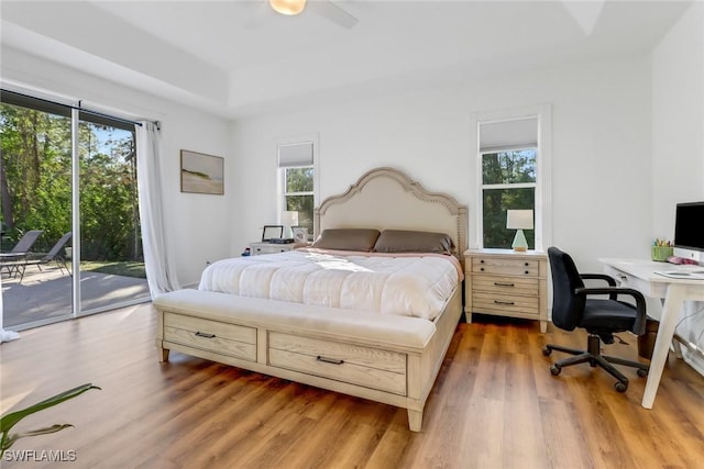 bedroom featuring access to outside, a raised ceiling, light wood-style flooring, and ceiling fan