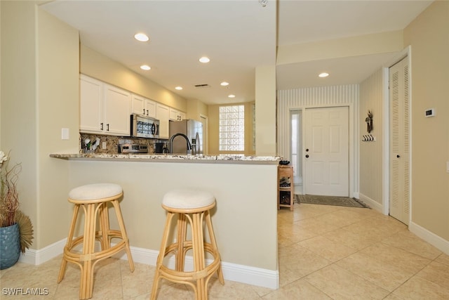 kitchen featuring a kitchen breakfast bar, tasteful backsplash, white cabinets, a peninsula, and stainless steel appliances