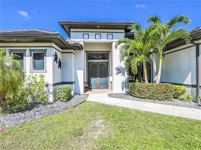 view of exterior entry featuring a yard, french doors, and stucco siding