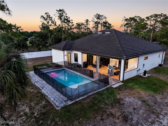 pool at dusk with a fenced backyard, a fenced in pool, a patio, and a yard