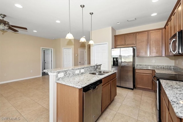 kitchen with ceiling fan, a kitchen island with sink, appliances with stainless steel finishes, a sink, and light stone counters