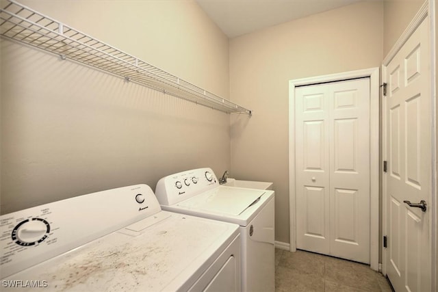 washroom featuring laundry area, baseboards, washer and clothes dryer, a sink, and light tile patterned floors