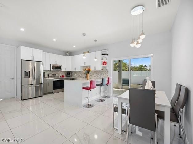 27257 Pinecrest Ln, Bonita Springs, FL 34135 - kitchen featuring visible vents, a peninsula, a kitchen bar, tasteful backsplash, and appliances with stainless steel finishes